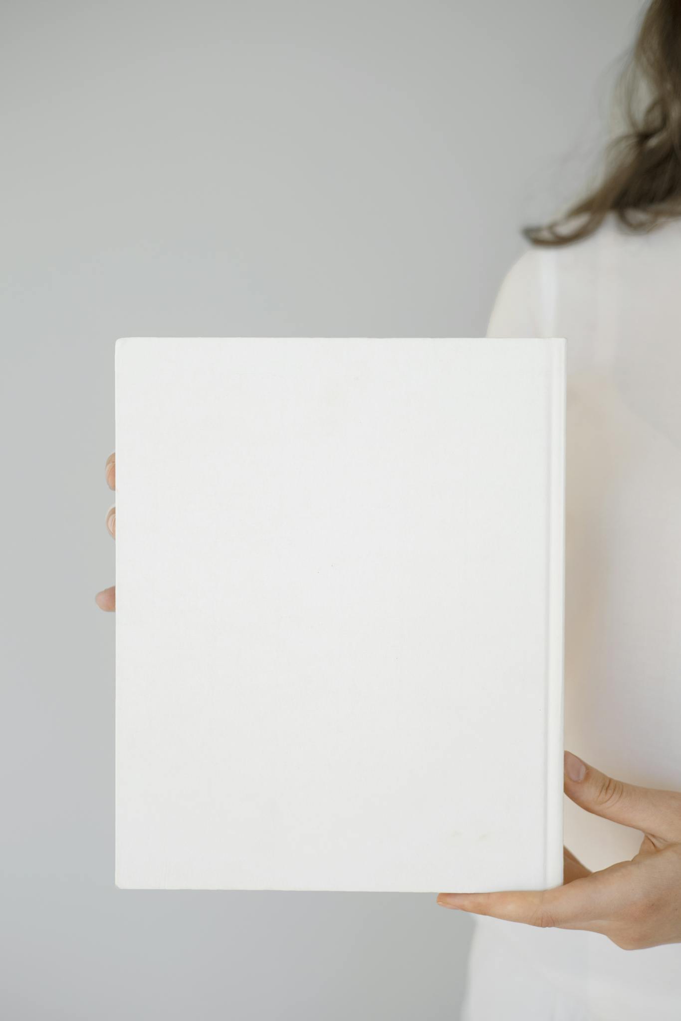 Minimalist close-up of a woman holding a blank white notebook, perfect for design mockups.